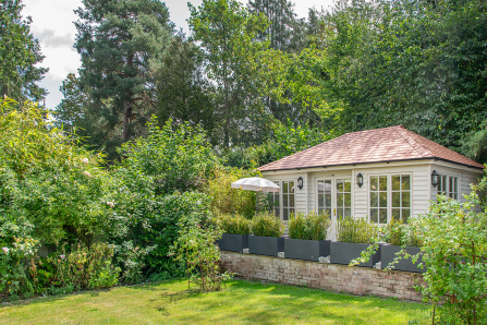 4.2 x 6.0m Garden Room Painted in Exterior Paint 'Sandstone' Traditional garden room surrounded by lush planting, with painted timber cladding, French doors, large windows and a cedar-shingle roof.